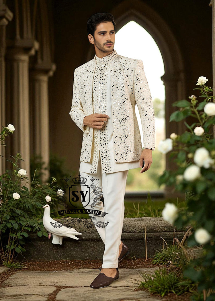 Man wearing a traditional white embroidered Prince jacket and pants standing in a garden with flowers and a stone archway.