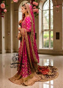 A timeless bridal dress design that exudes classic elegance and meticulous craftsmanship. The intricately crafted, opulent Banarsi Jamawar lehenga exudes a royal flair, with its heavy maroon and red borders creating a magnificent, flowing train.