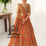 A stunning ensemble featuring Persimmon net blouse and an intricately embroidered Raw silk lehenga in the same vibrant hue. A shimmering kaamdani dupatta adds charm and sophistication to the ensemble.