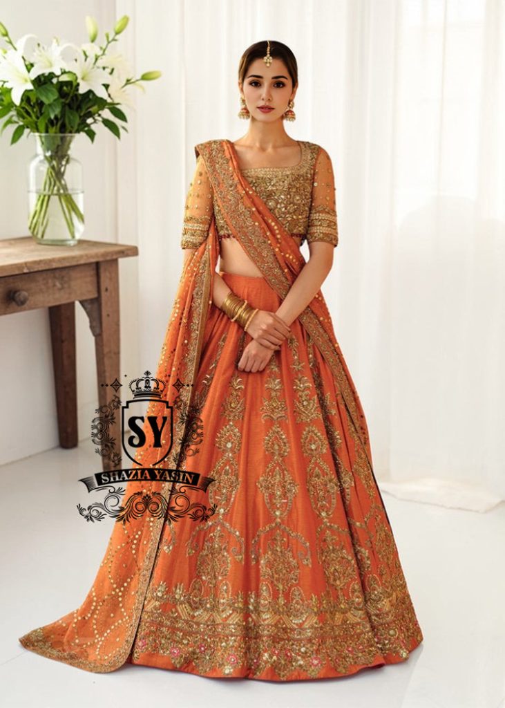 A stunning ensemble featuring Persimmon net blouse and an intricately embroidered Raw silk lehenga in the same vibrant hue. A shimmering kaamdani dupatta adds charm and sophistication to the ensemble.