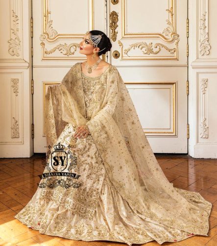 Bride in a traditional Ivory Hand Embellished wedding dress with sheer sleeves and floral decorations sitting in a decoratively paneled room.