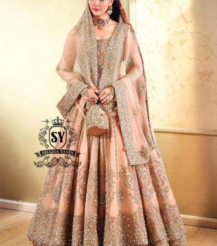 In a radiant shade of Peach puff, this bridal dress captures a timeless grandeur, sweetened with touches of pastel romance. This open-cut kalidaar gown shines with tissue silk lehenga.