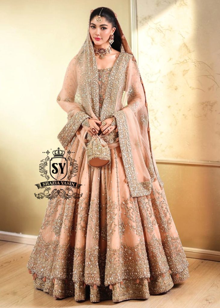 In a radiant shade of Peach puff, this bridal dress captures a timeless grandeur, sweetened with touches of pastel romance. This open-cut kalidaar gown shines with tissue silk lehenga.