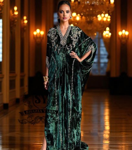 Woman in an elegant green Kaftan dress standing in a luxurious hallway with chandeliers.