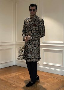 This luxurious royal black velvet sherwani, adorned with opulent gold hand embroidery, exudes a bold and dignified presence. The plush velvet fabric highlights the depth of the intricate hand embellishments, creating a truly regal style befitting a groom or a grand ceremony.