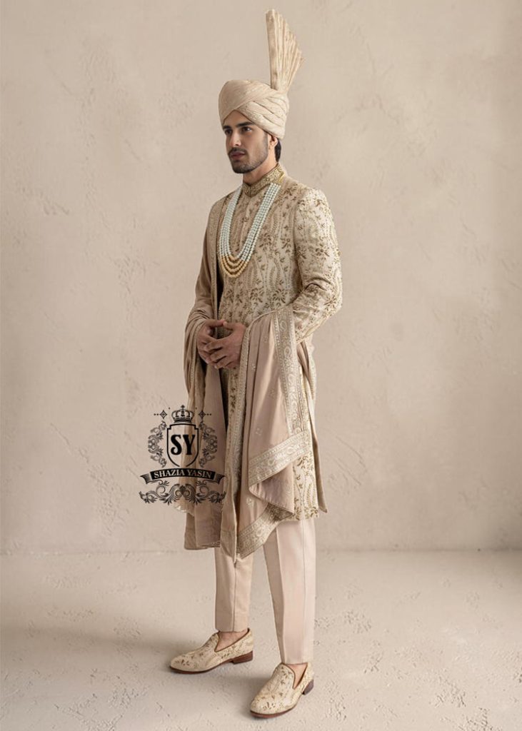 This sherwani is a masterpiece that blends timeless nobility with a modern sensibility. A finely hand-embroidered sherwani by Shazia Yasin, elevated with gold accents, paired with a statement mala, shawl and a bold turban for a timeless yet striking look.